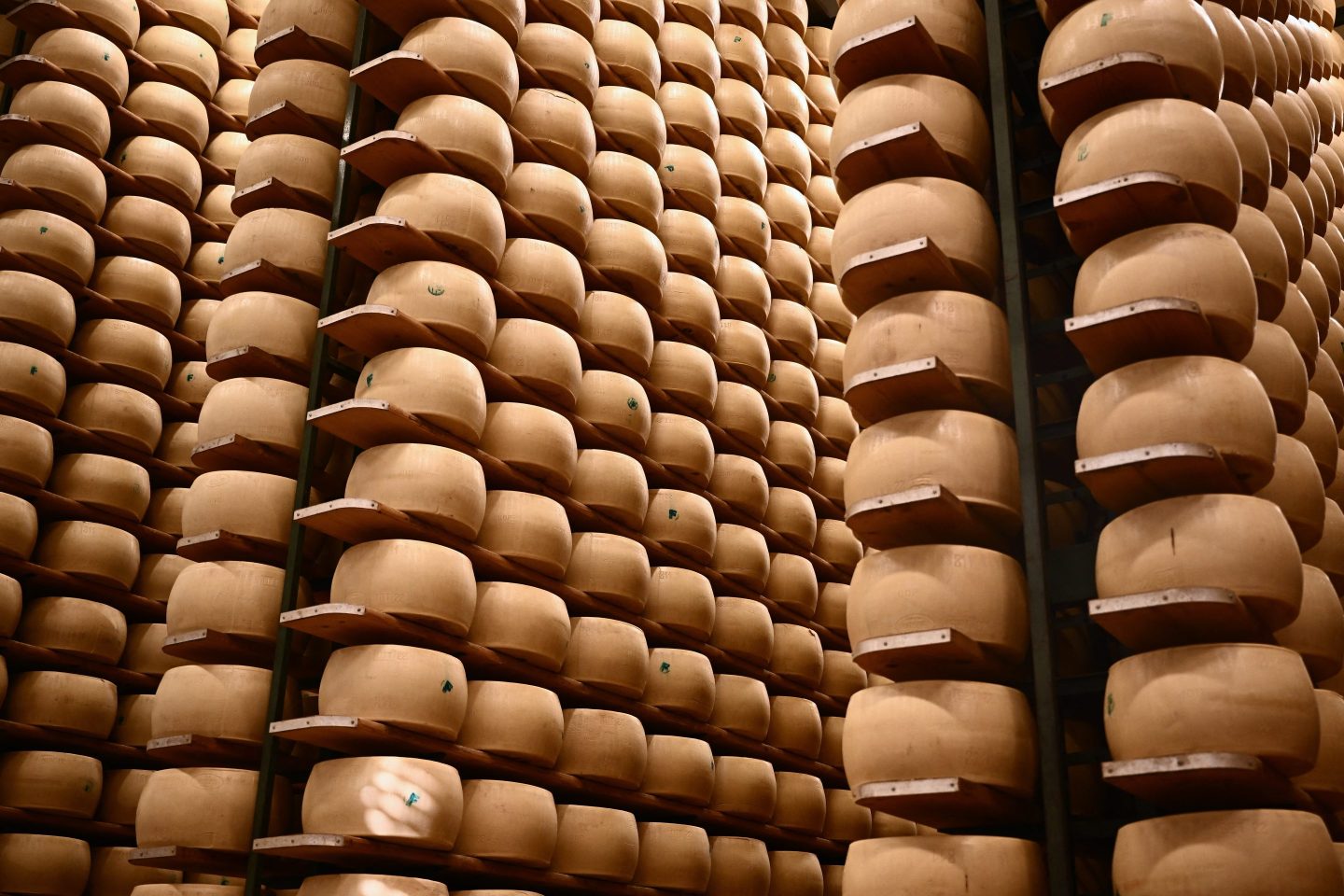 Rows of Parmigiano Reggiano wheels aging on wooden shelves in a climate-controlled warehouse in Emilia-Romagna
