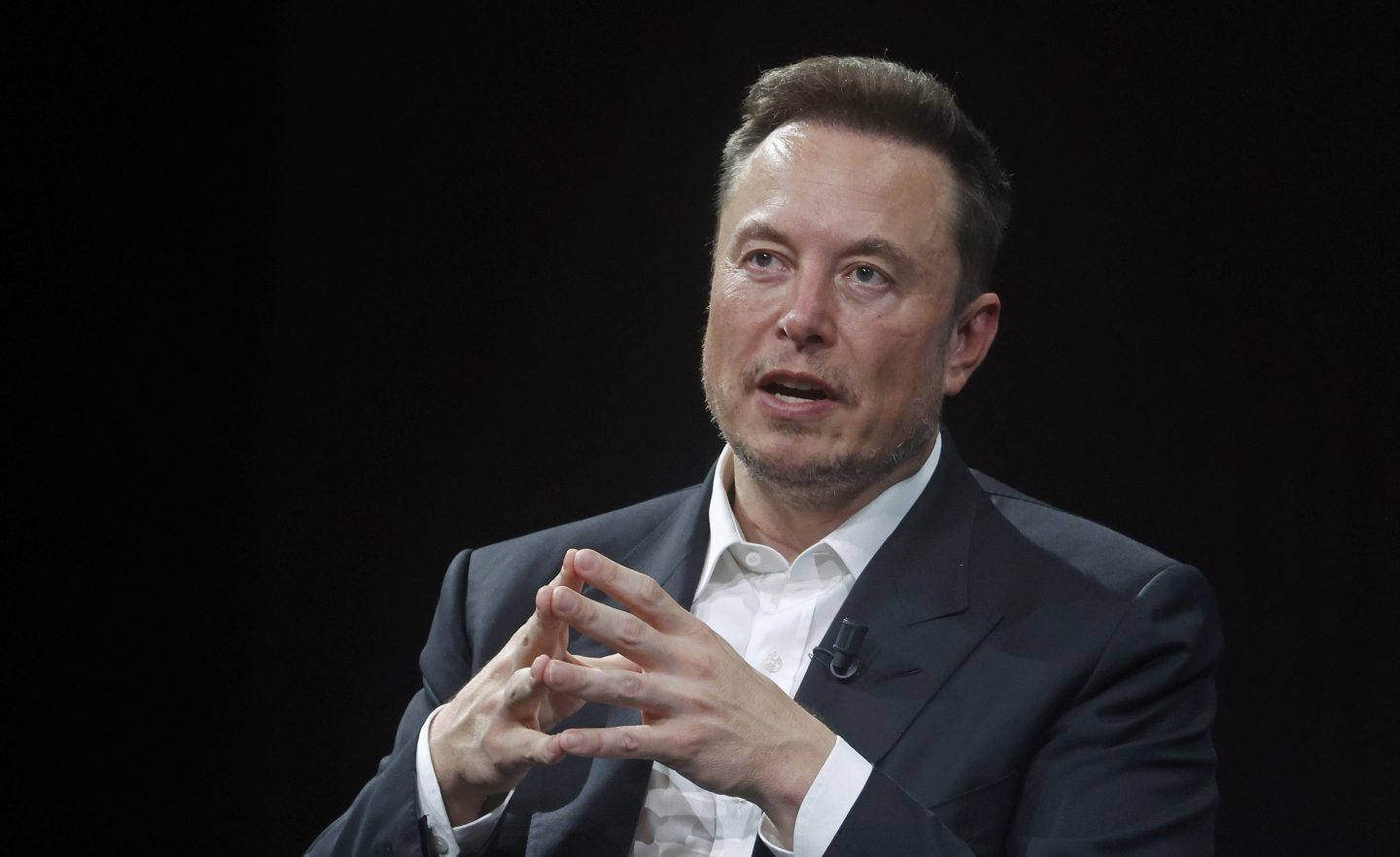 Elon Musk at a Tesla event, with a graphic of a pay scale showing disparity
