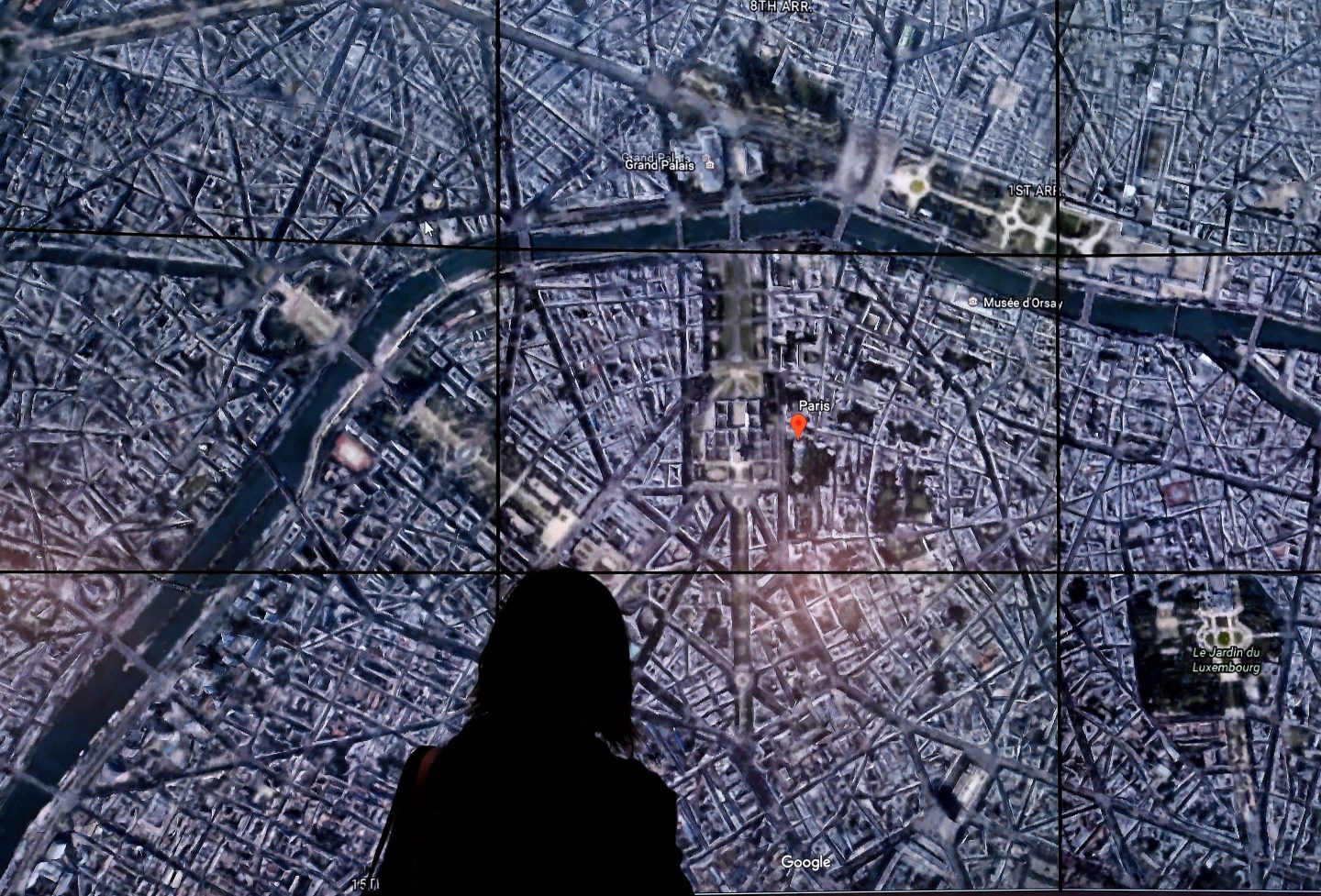 People look at a Google Earth map of Paris,France on a screen as Google Earth.